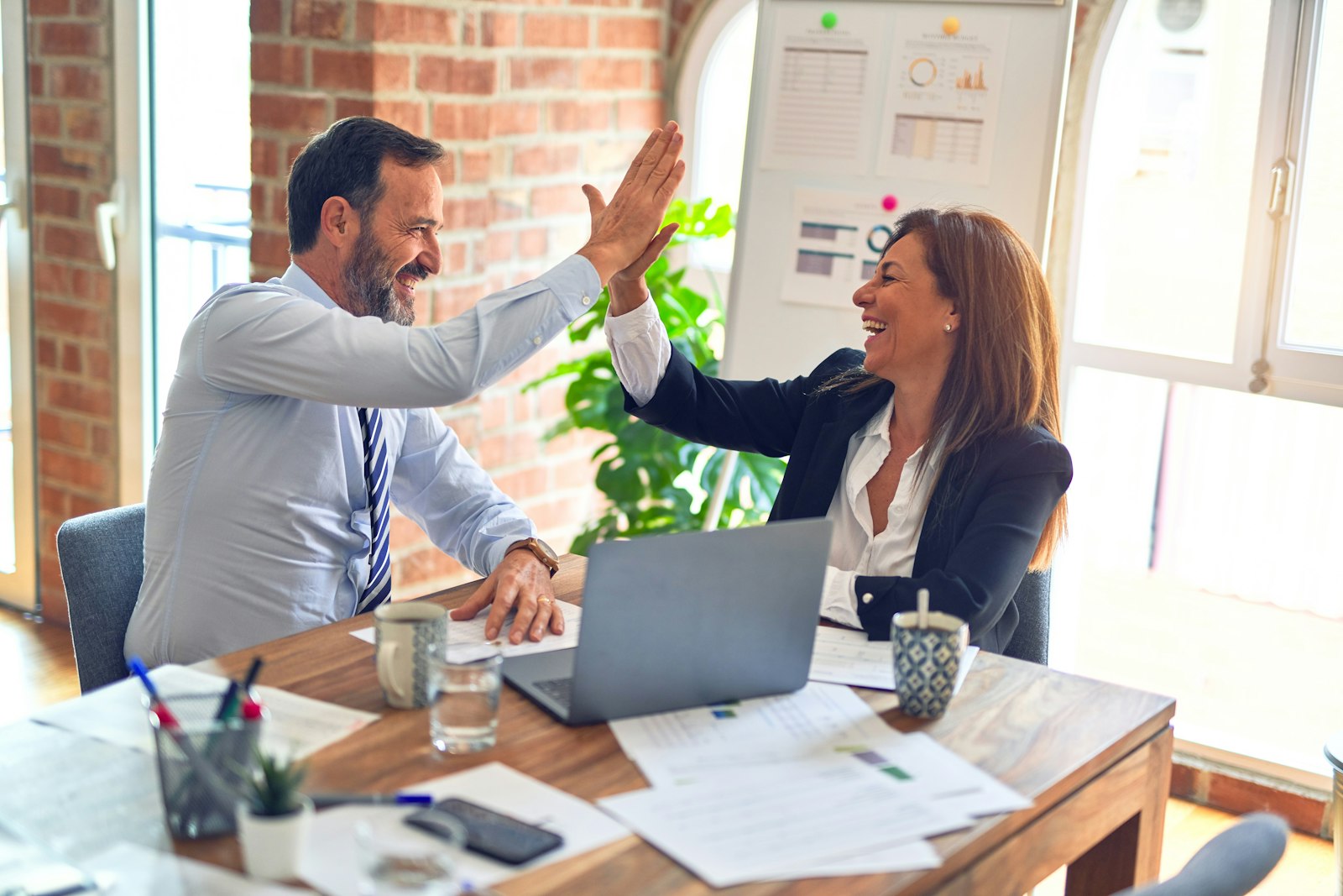 Two colleagues celebrating a win with a high five at their desk